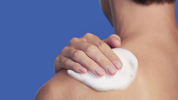 un homme appliquant du gel douche sur son epaule
